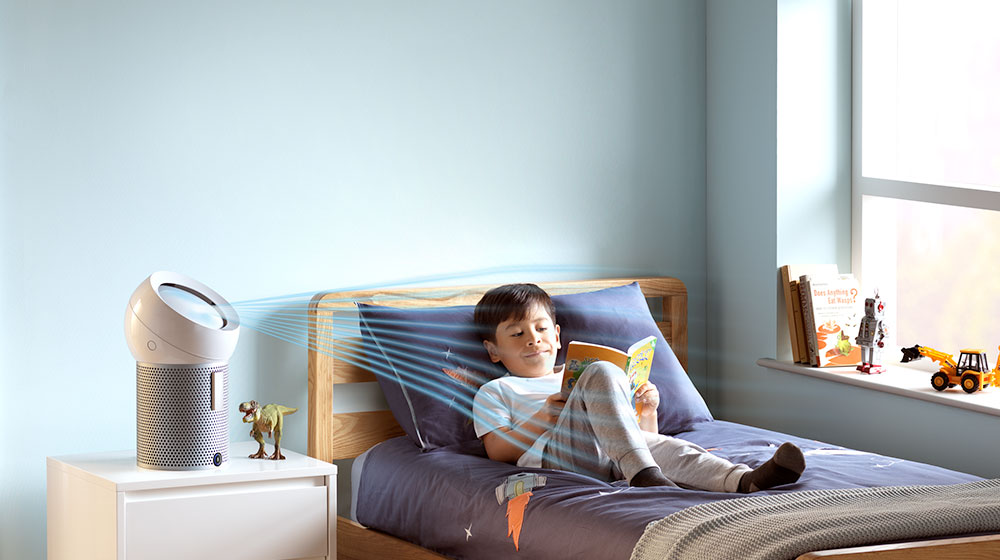 A boy reads on his bed, while a Dyson personal purifier fan projects cooling airflow at him